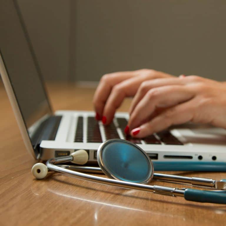 typing on laptop. a stethoscope sits on the desk.