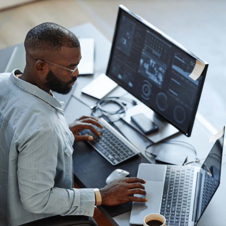 man working in an office with a laptop and a monitor